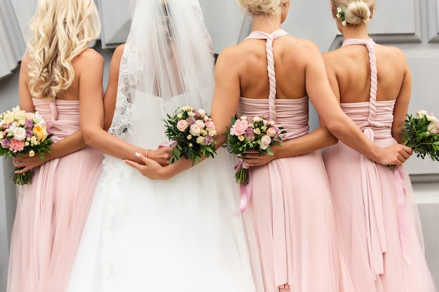 Braut und Brautjungfern in rosa Kleidern umarmen sich und posieren mit Blumensträußen am Hochzeitstag