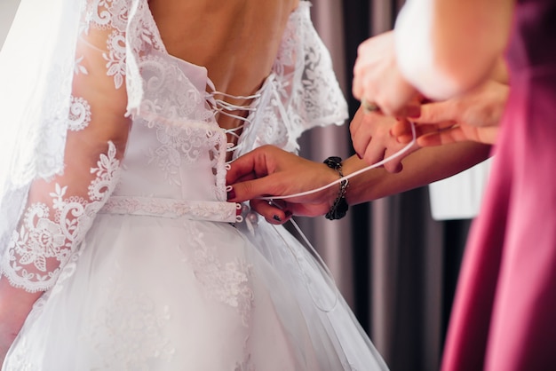 Brautjungfern schnüren sich weißes Hochzeitskleid auf dem Rücken der Braut