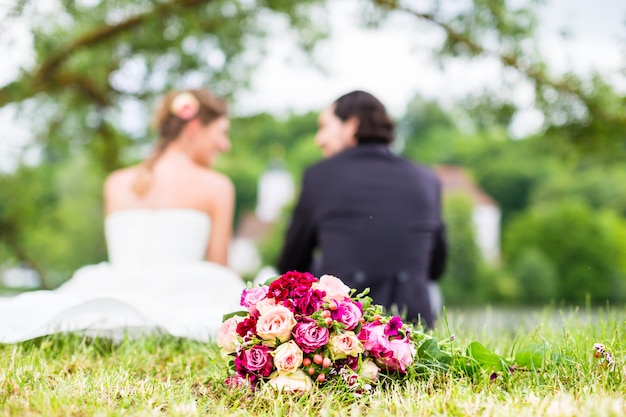 Brautpaare mit dem Blumenstrauß, der auf Wiese sitzt