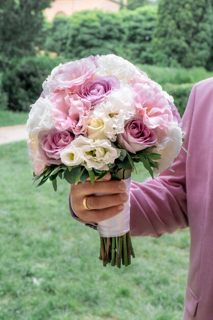 Brautstrauß aus rosa, weißen und lila Rosen in der Hand des Bräutigams.