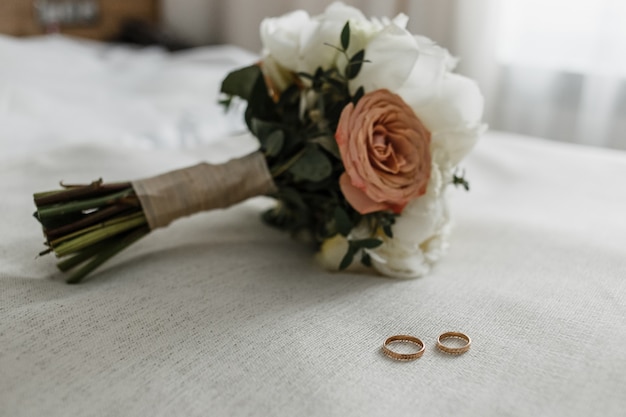 Brautstrauß mit beigen und cremigen Rosen und Brautringen auf weißem Bett