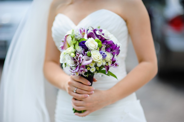 Brautstrauß von lila und weißen Blumen in den Händen der Braut