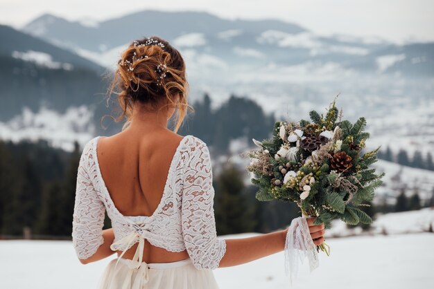 Brautwinter im weißen Hochzeitskleid, das Blumenstrauß in den Händen hält