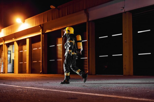 Bravo bombeiro em uniforme de proteção com equipamento completo funcionando para cuidar do fogo.