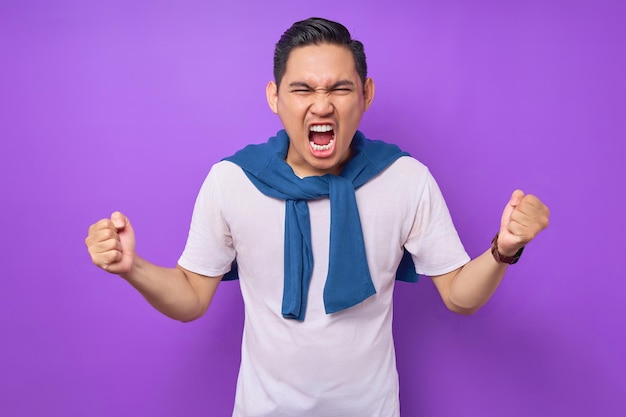 Bravo e estressado jovem asiático vestindo camiseta branca espalhando as mãos gritando e gritando isolado sobre o conceito de estilo de vida de pessoas de fundo roxo