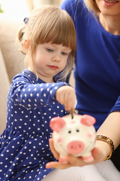 Brazo de niña pequeña poniendo monedas de dinero pin en retrato de ranura de lechón cara rosa feliz.