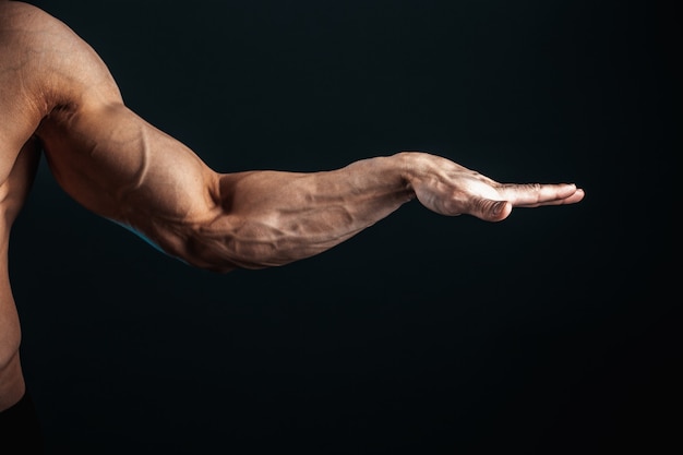 Foto brazo tenso, venas, músculos de culturista en un espacio oscuro, aislar