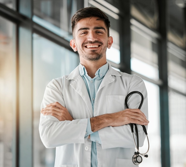 Brazos cruzados felices y retrato de un médico varón con un estetoscopio en un hospital médico Sonrisa de confianza y joven profesional trabajador de la salud o cirujano con orgullo en la clínica de medicare