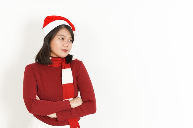 Brazos cruzados y mirando a un lado de la hermosa mujer asiática vestida con cuello alto rojo y gorro de Papá Noel