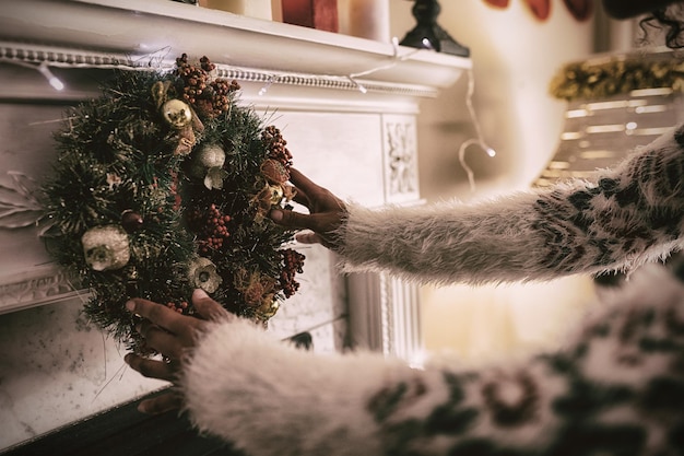 Brazos de una mujer de raza mixta en su salón en Navidad, arreglando una ofrenda floral en una repisa de la chimenea