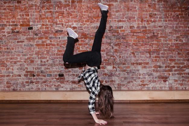 Breakdance é vida. Felicidade em se mover. Adolescente desportiva, fundo de parede de tijolo com espaço livre. Estilo de vida hip hop, dança flexível, jovem fêmea, conceito de movimento