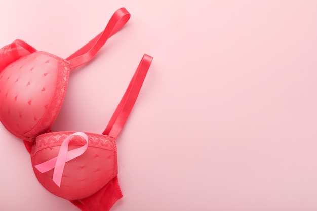 Breast Cancer Awareness Ribbon Roter BH und rosa Schleifenband liegen auf weiblichem BH auf Hintergründen Brustkrebsbewusstsein und Oktober Pink Day Weltkrebstag Draufsicht Mock up