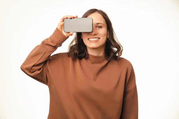 Breit lächelnde frau bedeckt ein auge mit ihrem telefonbildschirm mit kopierraum
