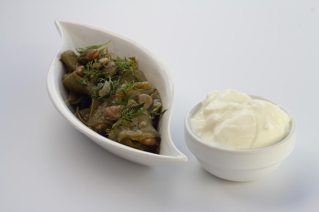 Breite Bohnen und Dill auf dem weißen Teller mit weißem Hintergrund mit Joghurt
