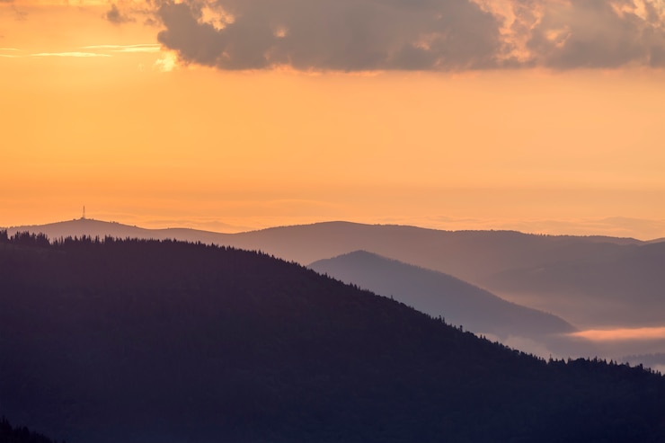 Foto breites panorama von nebeligen bergen bei sonnenuntergang auf hellem klarem orange himmel