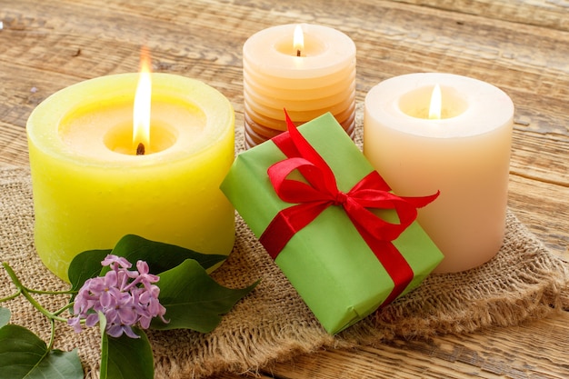 Brennende Kerzen, Geschenkbox und lila Blumen auf Sackleinen und alten Holzbrettern.