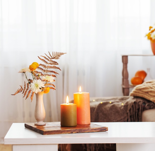 Brennende Kerzen mit Herbstdekor auf weißem Tisch zu Hause