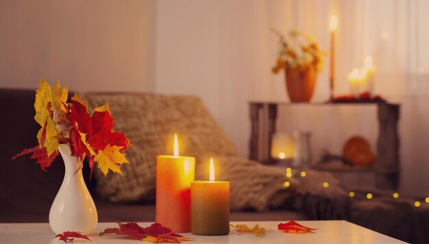 Brennende Kerzen mit Herbstdekor auf weißem Tisch zu Hause