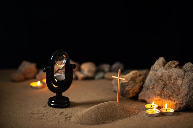 Brennende Kerzen mit Steinen und kleinem Grab auf Sand als Erinnerung an den Tod der Beerdigung