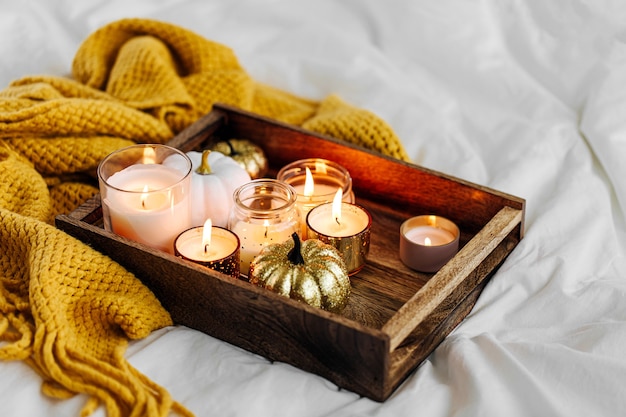 Brennende Kerzenkürbisdekoration auf Holztablett mit warmem Plaid im Bett. Herbst-Stil. Hygge-Konzept.