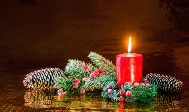 Foto brennende rote kerze in einem weihnachtskranz aus fichtenzweigen und zapfen.