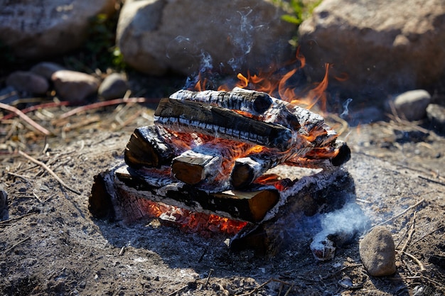 brennendes Brennholz und Kohlen mit einer großen Flamme mit Rauch im Freien