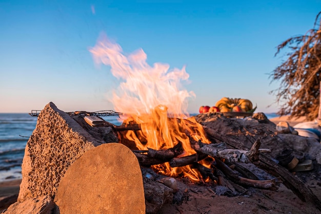 Brennendes Holz im Kamin neben Früchten am Strand gegen den klaren blauen Himmel am Abend