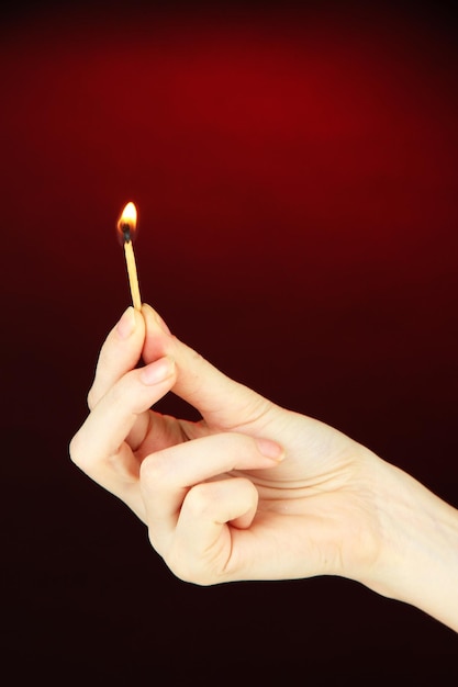 Brennendes Streichholz in weiblicher Hand auf dunkelrotem Hintergrund