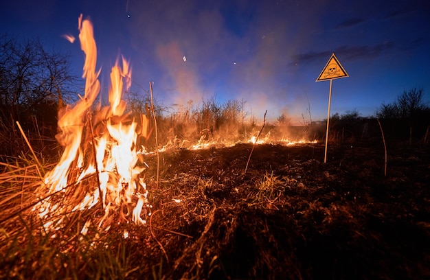 Brennendes trockenes Gras und Warnschild im Feld bei Nacht