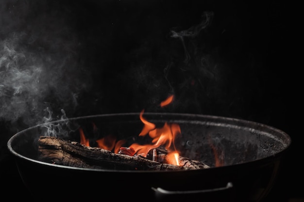 Brennholz brennt nachts in einem runden Grill Dunkler Hintergrund Vorbereitung zum Kochen von Speisen auf dem Grill