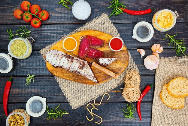 Bresaola curada fatiada com especiarias e um raminho de alecrim em fundo rústico de madeira escuro.