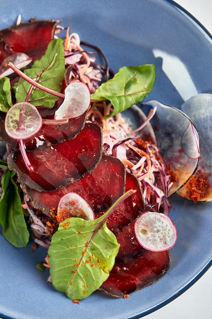 Bresaola, dünn geschnitten mit Salat Italiana geheilt gesalzenes Rindfleisch in einem Teller mit Sauce und Rote-Bete-Blättern Nahaufnahme.