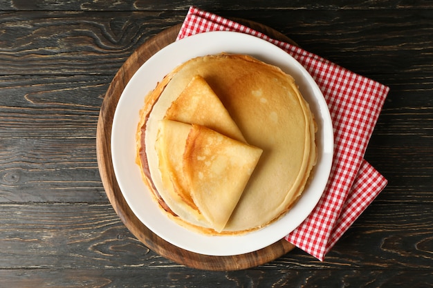 Brett mit dünnen Pfannkuchen auf hölzernem Hintergrund