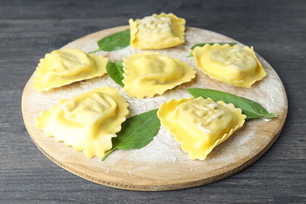 Brett mit rohen Ravioli auf dunklem Holzhintergrund