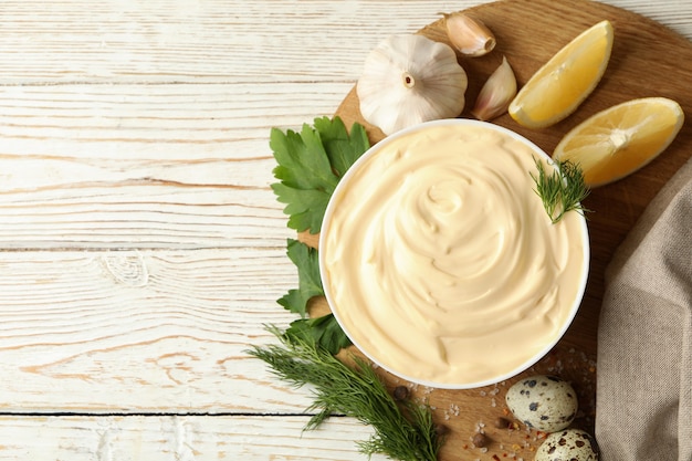 Brett mit Schüssel Mayonnaise und Zutaten zum Kochen auf hölzernem Hintergrund