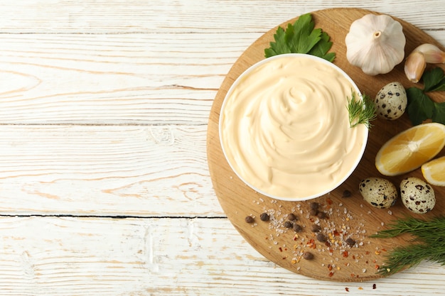 Brett mit Schüssel Mayonnaise und Zutaten zum Kochen auf hölzernem Hintergrund