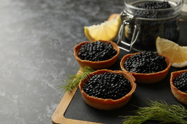 Foto brett mit törtchen und glas mit kaviar auf schwarzem rauch