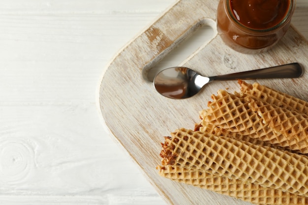 Brett mit Waffelröllchen mit Kondensmilch auf Holz