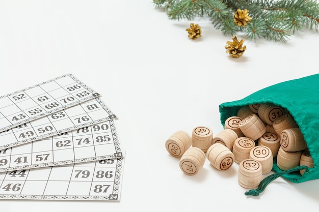 Brettspiel Lotto. Lottofässer aus Holz mit grüner Tasche und Spielkarten. Weihnachtstannenzweige im Hintergrund. Geringe Schärfentiefe