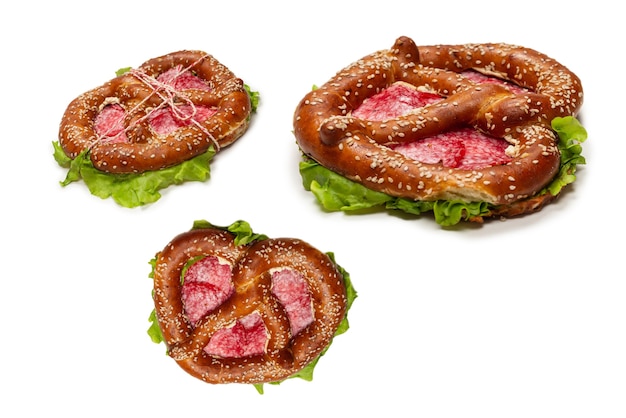 Brezel mit Salami und Salat auf einem weißen Hintergrund. Leckerer Imbiss.