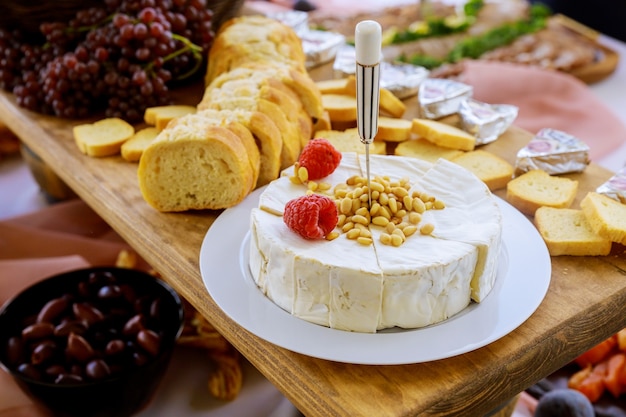 Briekäse mit Nüssen, Brot und Trauben auf rustikalem Holztisch.