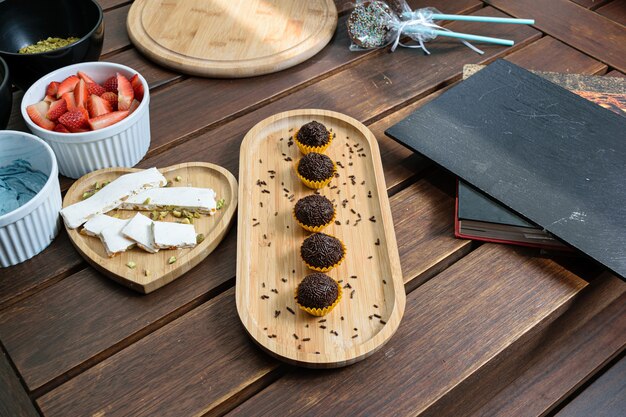 Brigadeiros alinharam-se ao lado do pistache Turron em uma mesa de madeira. Ao lado de creme de manteiga, morangos, pistache, pirulito de chocolate e um livro.