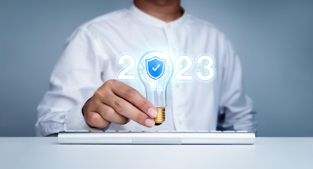 Brilhando 2023 ano civil números estilo neon com ícone de escudo de segurança cibernética na lâmpada de tendência criativa segurando pelo empresário com computador teclado Feliz ano novo de 2022 com conceito de tecnologia