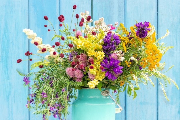 Brilhante colorido buquê de flores silvestres em starm lata pode vaso em placas de madeira de fundo azul