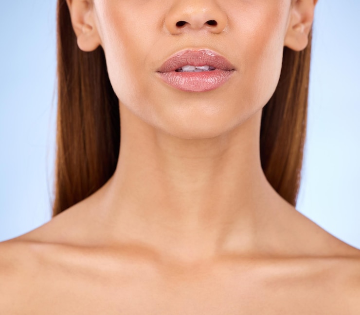 Foto brilho de lábios e beleza com rosto e mulher em close para cuidados cosméticos e batom em fundo azul dermatologia de brilho de pele e cuidados com a pele feminino com preenchimento labial e facial com maquiagem em estúdio