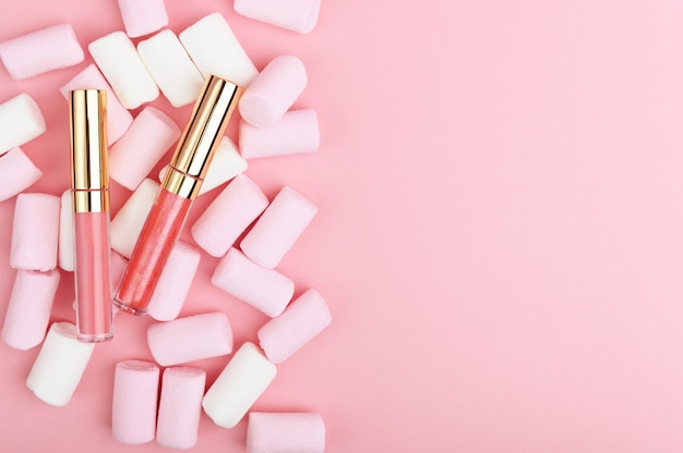 Brilho labial rosa pastel sobre um fundo de doces.