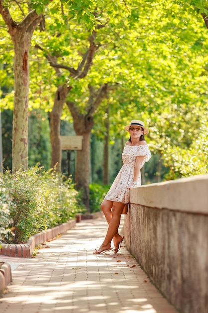 La brillante y hermosa chica con un vestido ligero y un sombrero camina por un callejón de árboles en Mónaco en un clima soleado