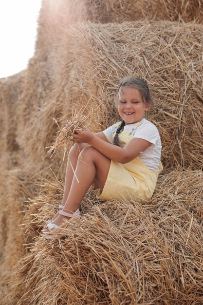 Brillante hermosa niña en pajar sonriendo mirando hacia abajo y con algo de heno en las manos usando