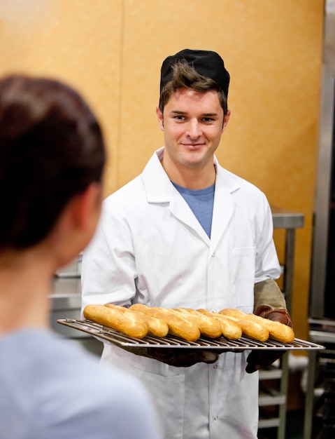 Brillante joven panadero macho con baguettes en la cocina