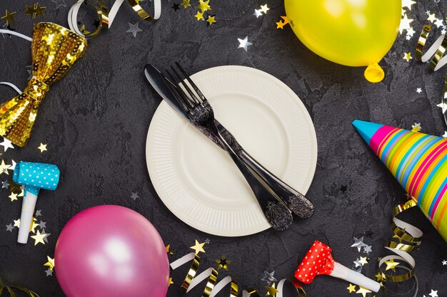 Foto brillante mesa festiva de carnaval con plato y cubiertos en la mesa de piedra negra decorada con accesorios de fiesta
